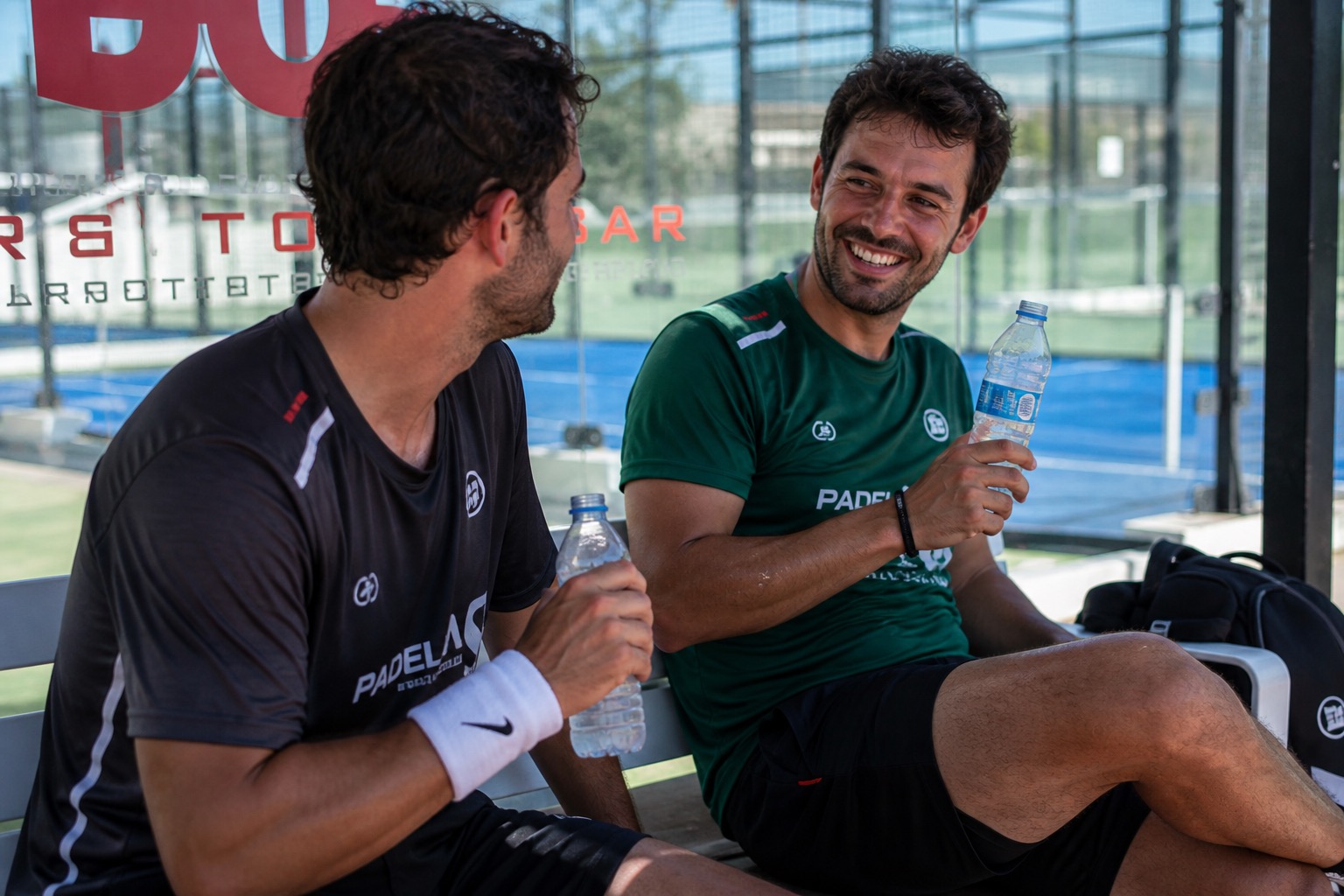 Jugadores de pádel tomando agua a la sombra de la pista en un descanso de partido veraniego