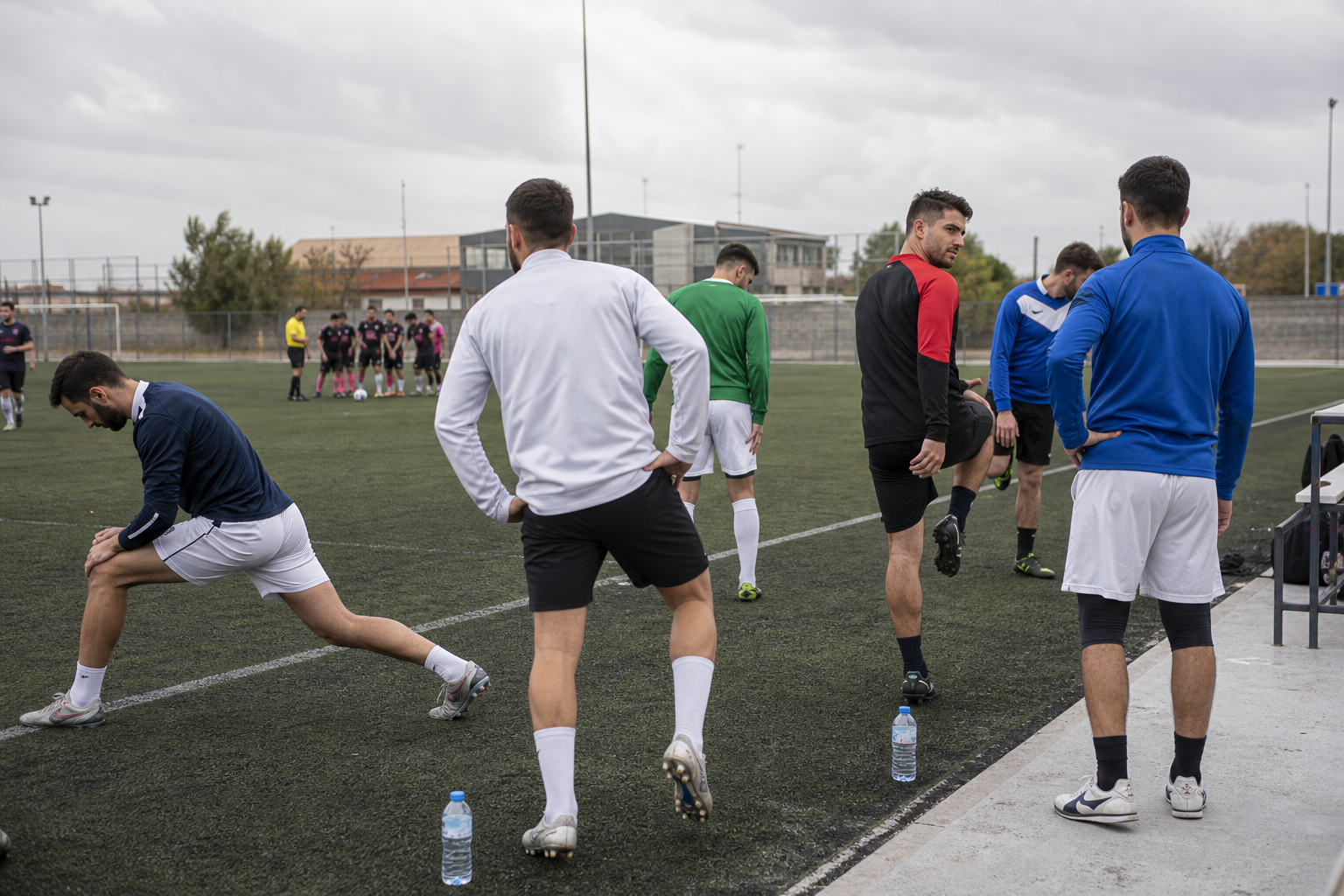 Jugadores amateur calentando en la banda de un campo municipal visitante
